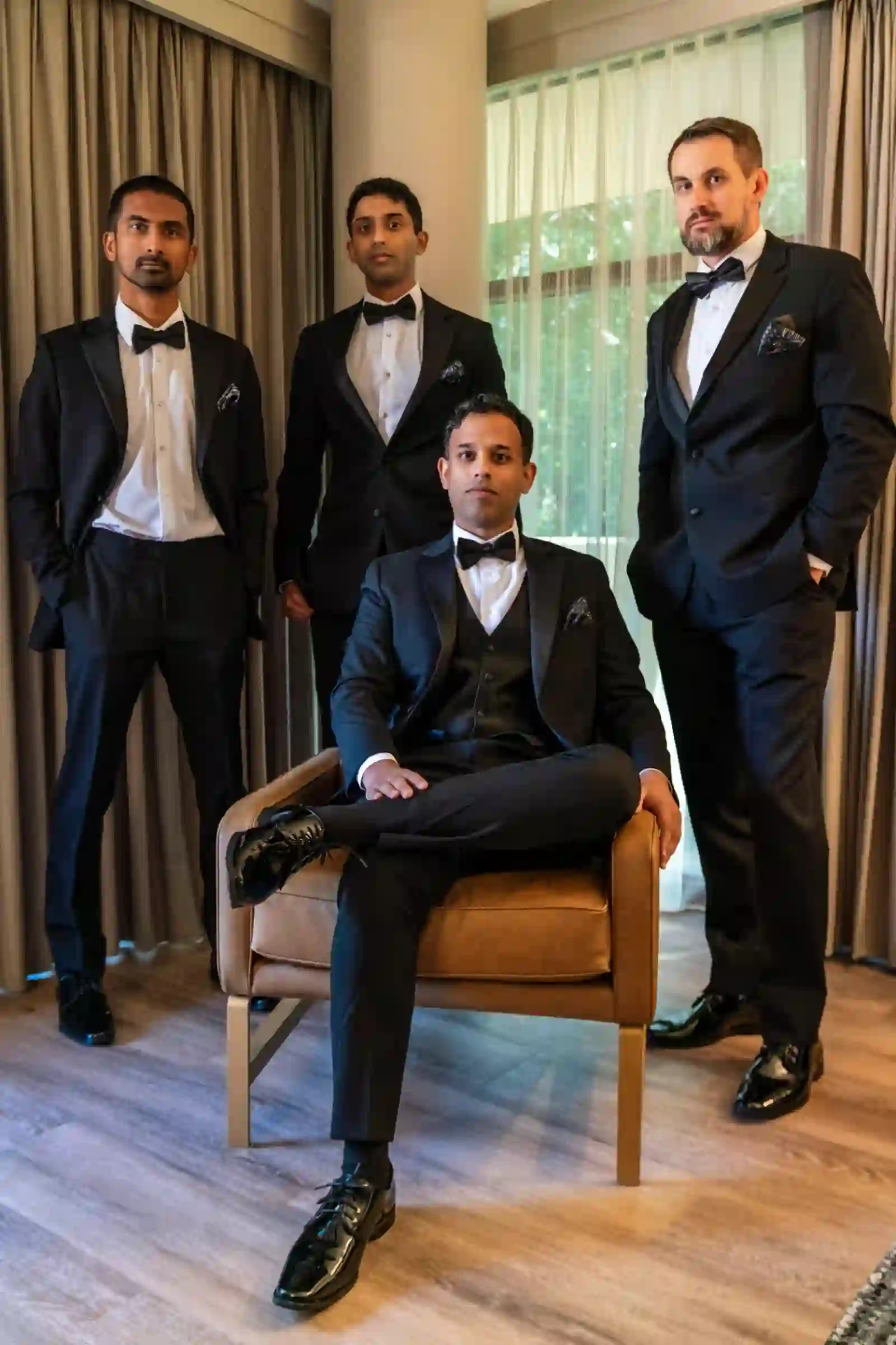 Groom seated with his groomsmen in tailored black tuxedos in the suite