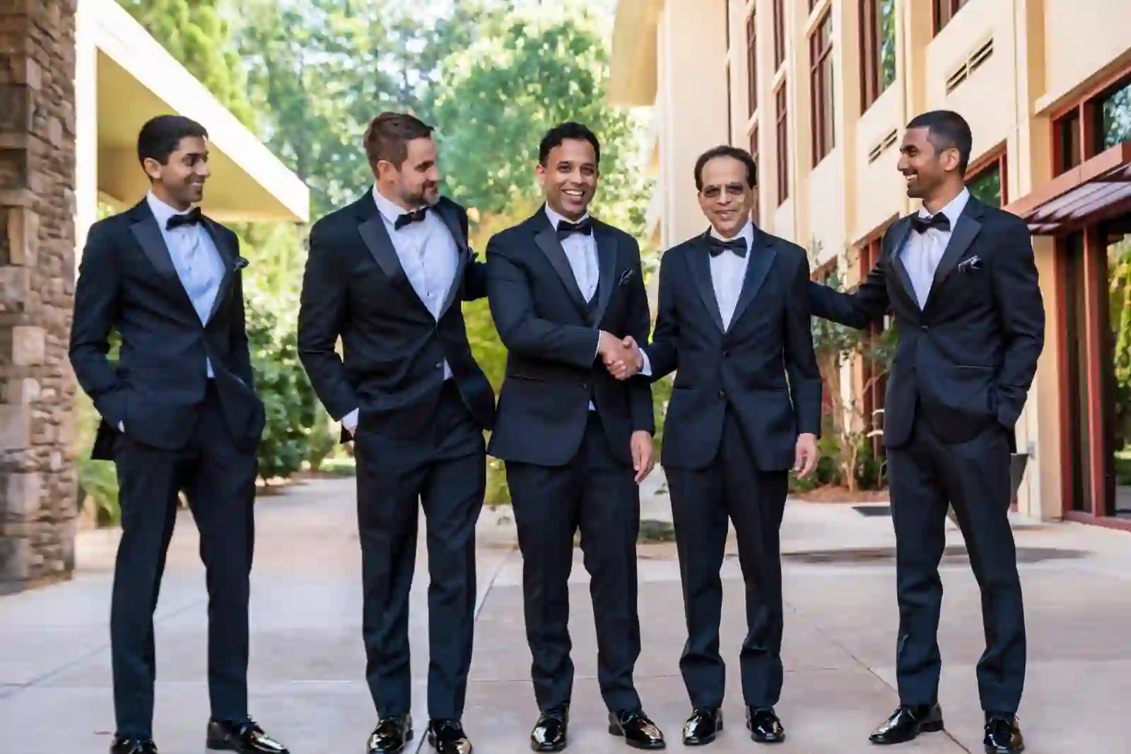 Groom shaking his father's hand surrounded by groomsmen outside the venue