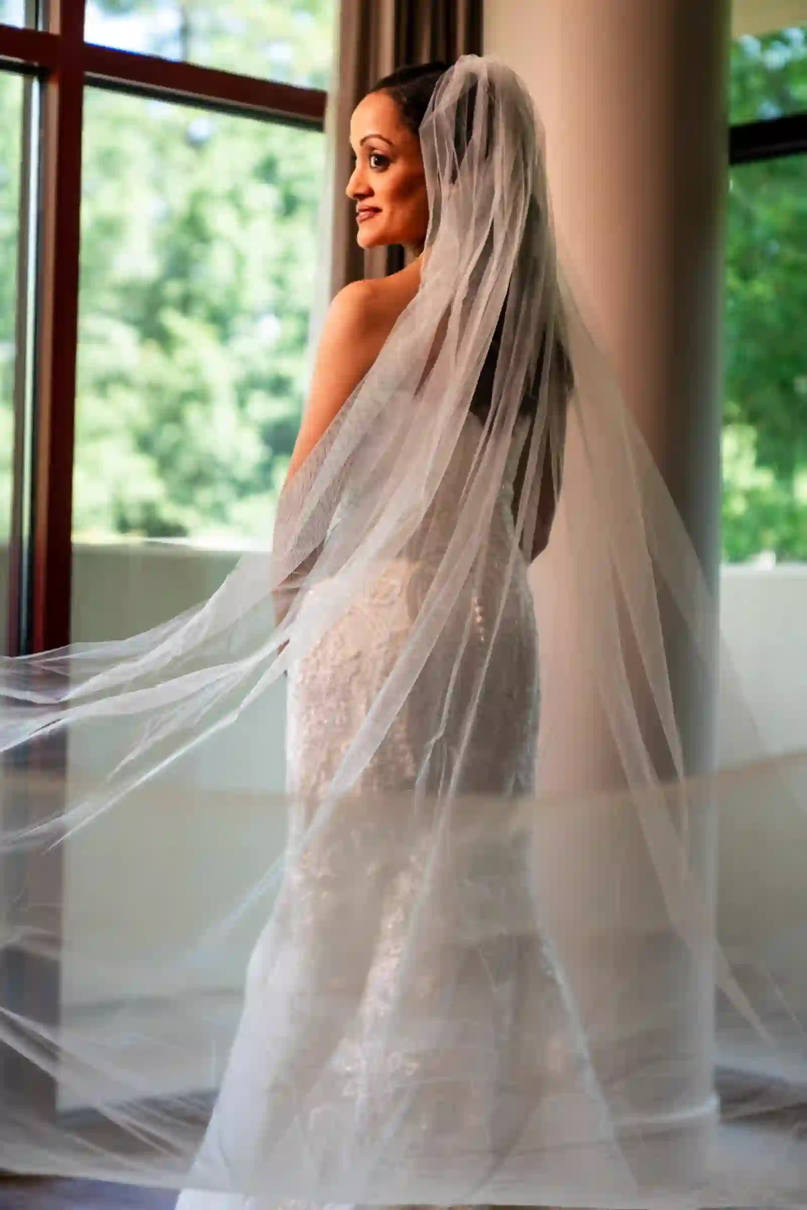 Bride glancing back over her shoulder, cathedral veil sweeping behind a beaded lace gown