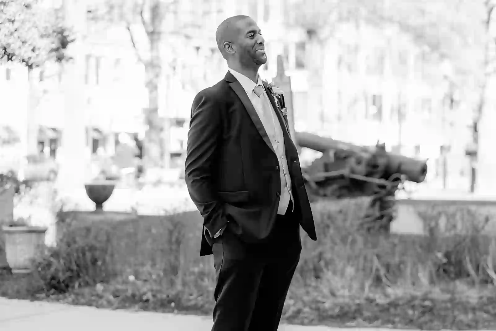 Black and white portrait of the groom in a tuxedo standing in a city park