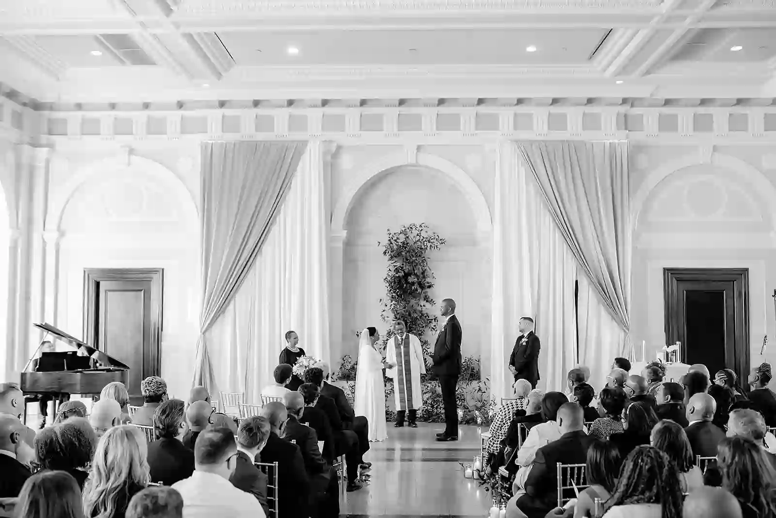 Black and white ceremony in a grand marble hall with draped columns and greenery backdrop