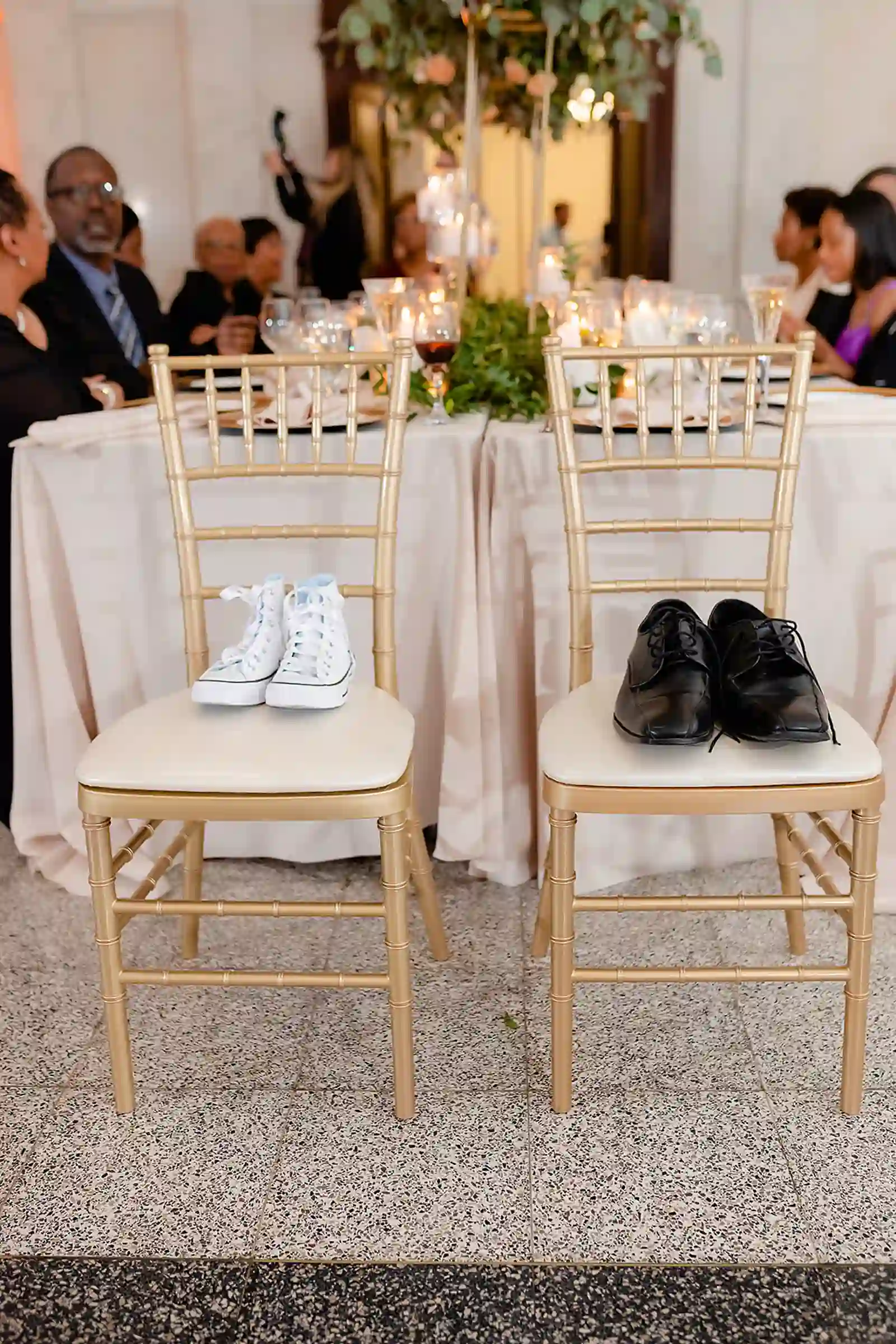 Two gold chiavari chairs holding the couple's wedding sneakers and dress shoes as a tribute