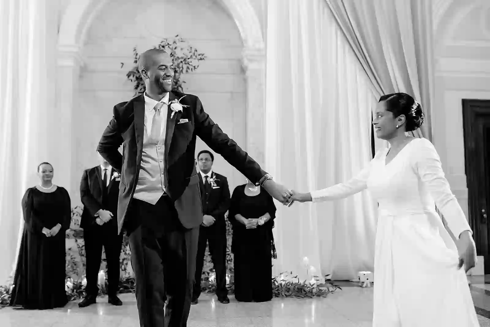 Black and white first dance moment with the groom twirling the bride as guests look on