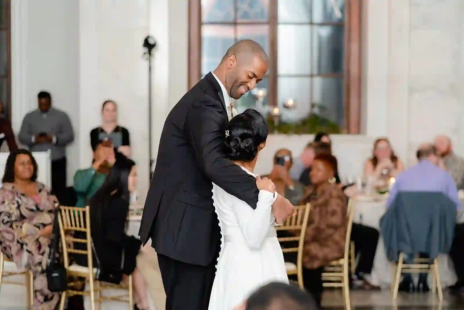 Close, candid embrace during the reception with guests watching from gilded tables