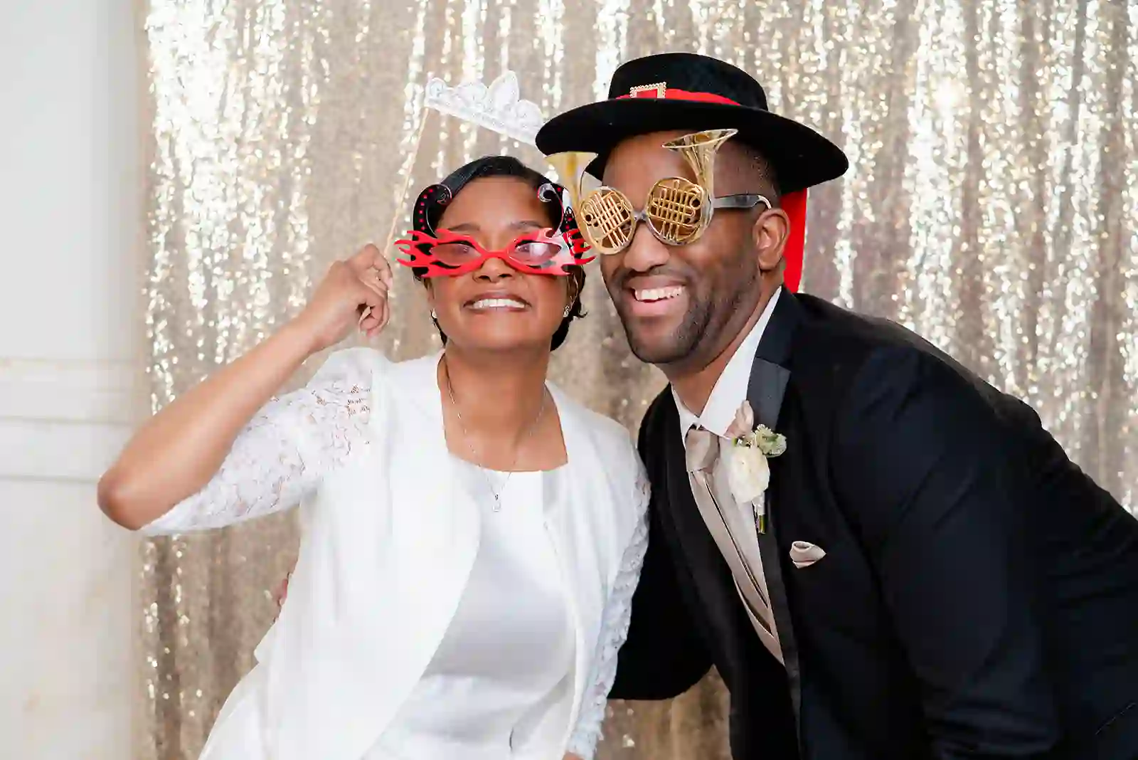 Joyful photo booth moment with playful props against a champagne sequin backdrop