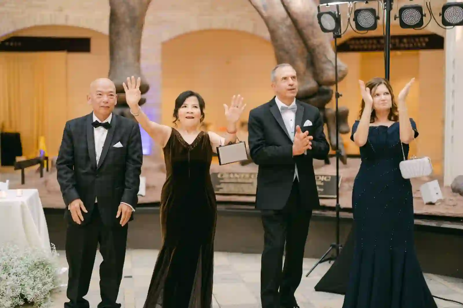 Both sets of parents waving and applauding beneath the museum's dinosaur display
