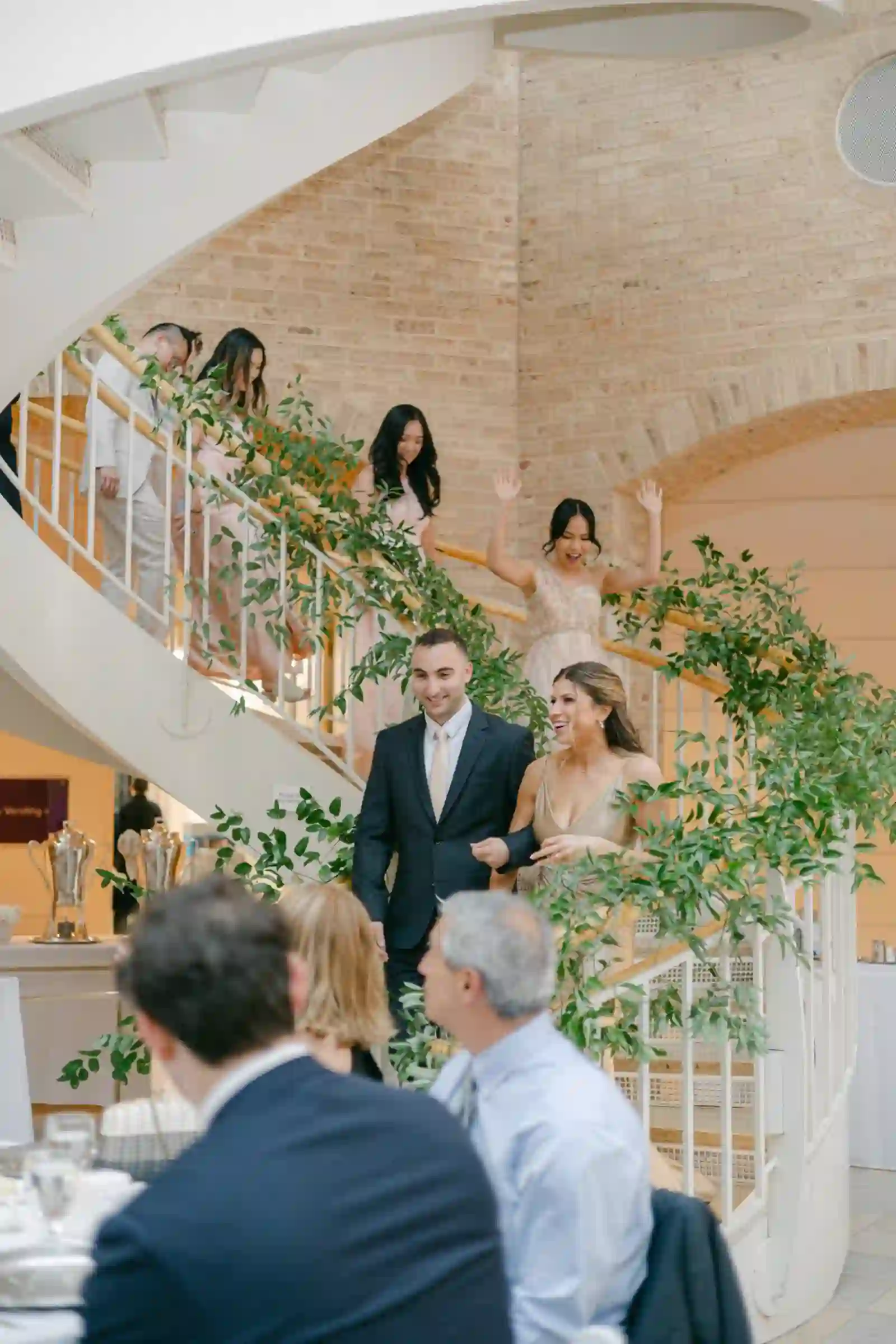 Bridal party descending a greenery-wrapped spiral staircase into the reception