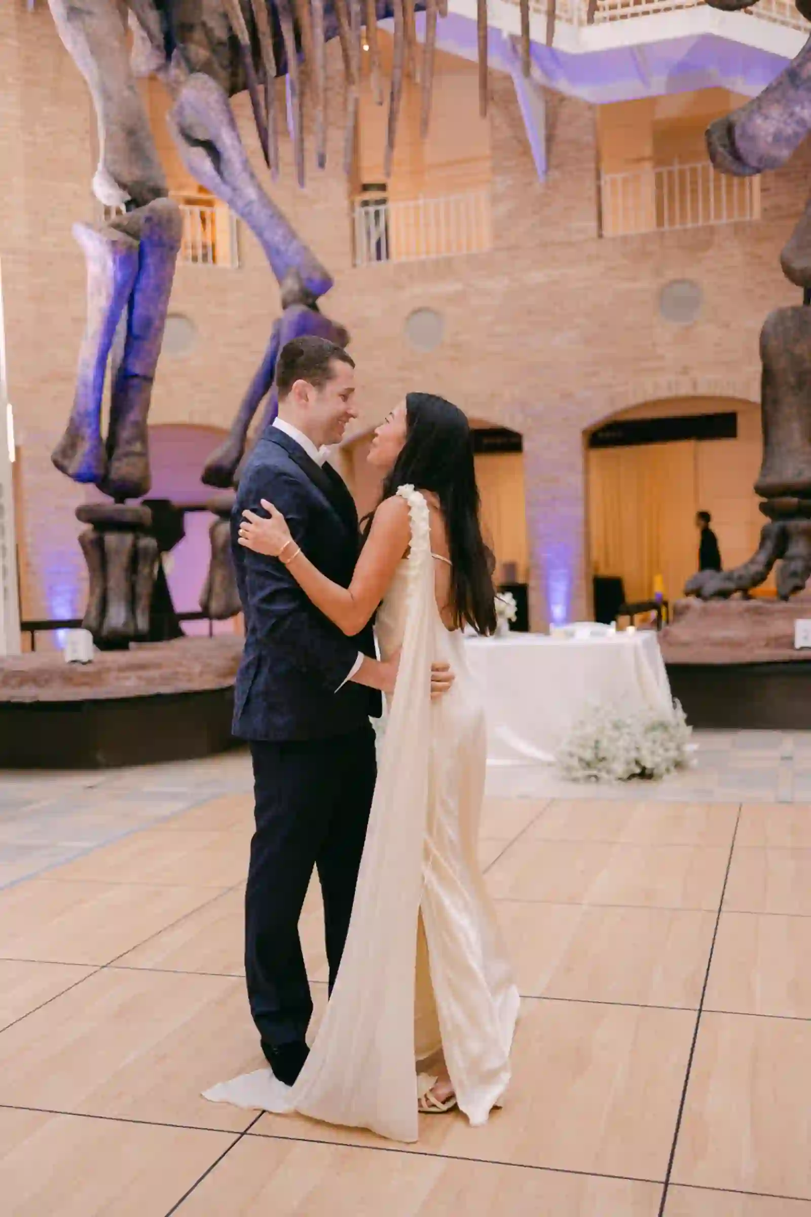 Tender first dance embrace under museum dinosaur fossils with violet uplighting