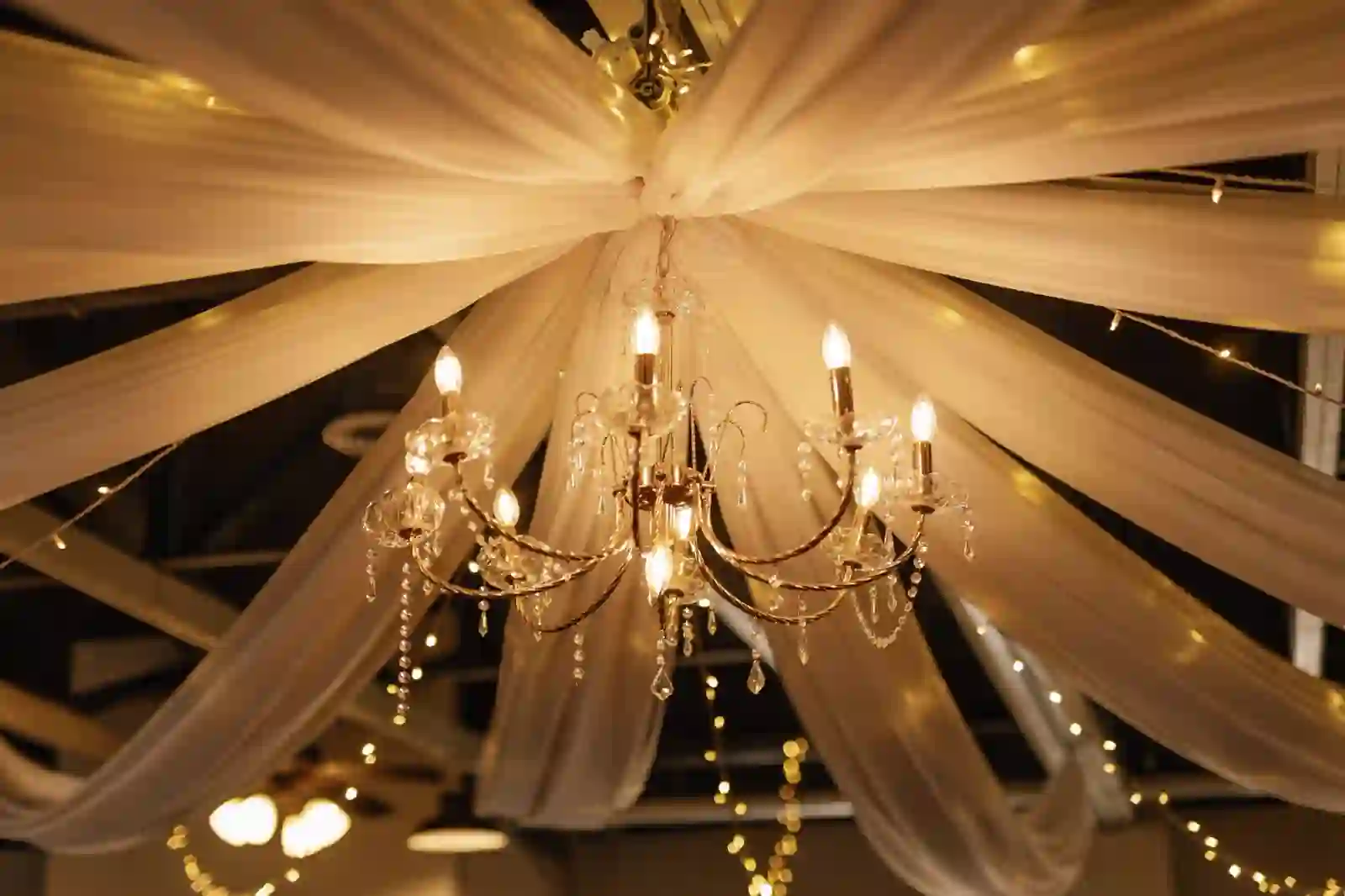 Crystal chandelier draped with white fabric and warm fairy lights