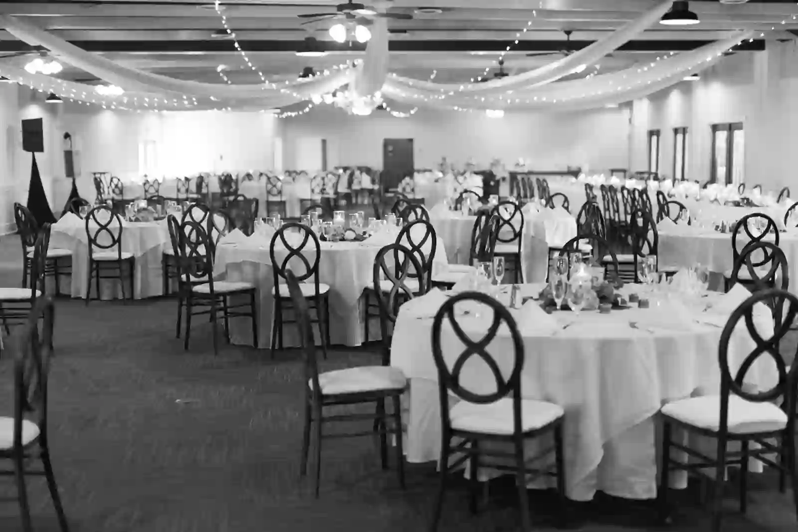 Black and white reception hall with draped fabric and string lights overhead