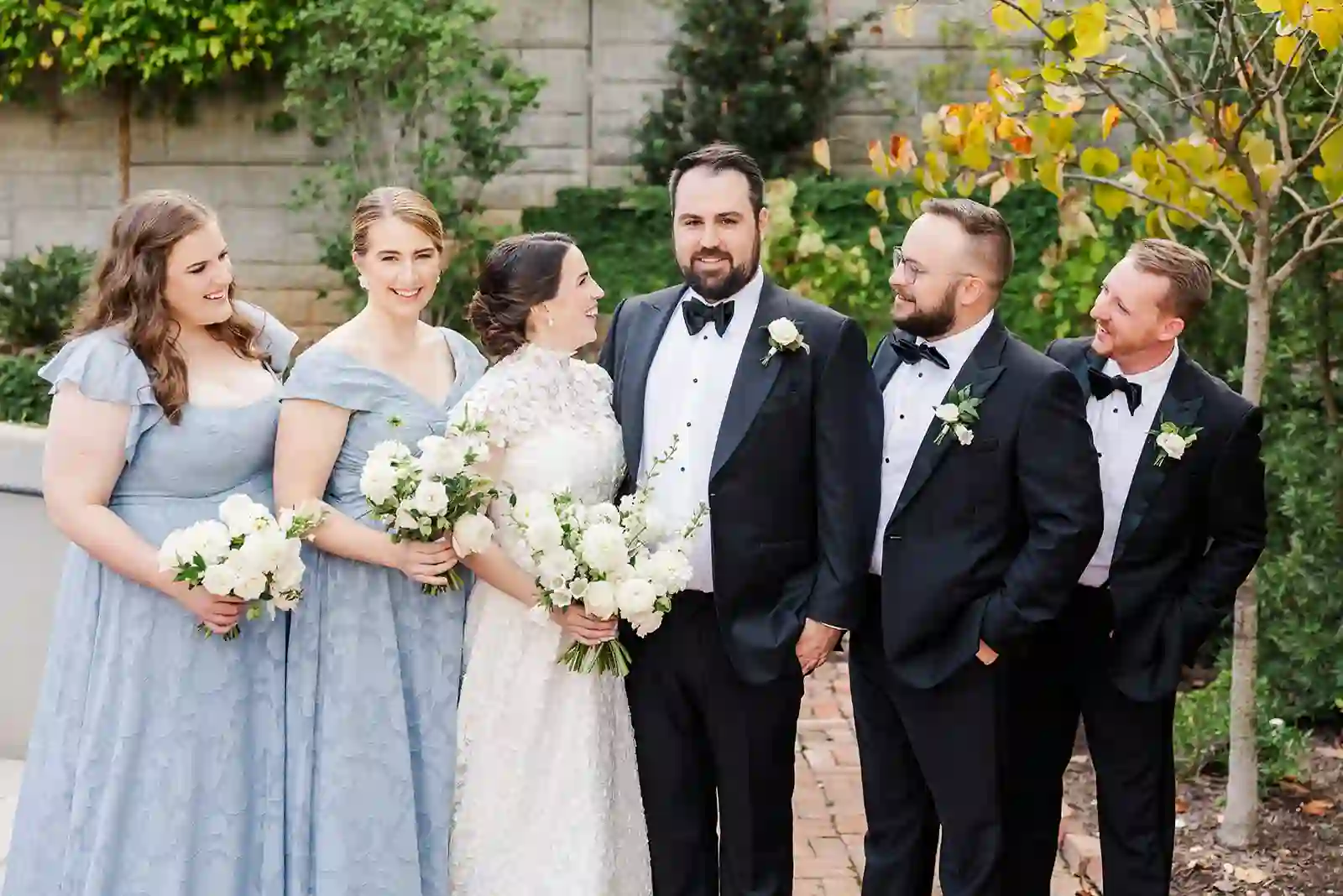 Wedding party laughing together in a brick courtyard beneath string lights