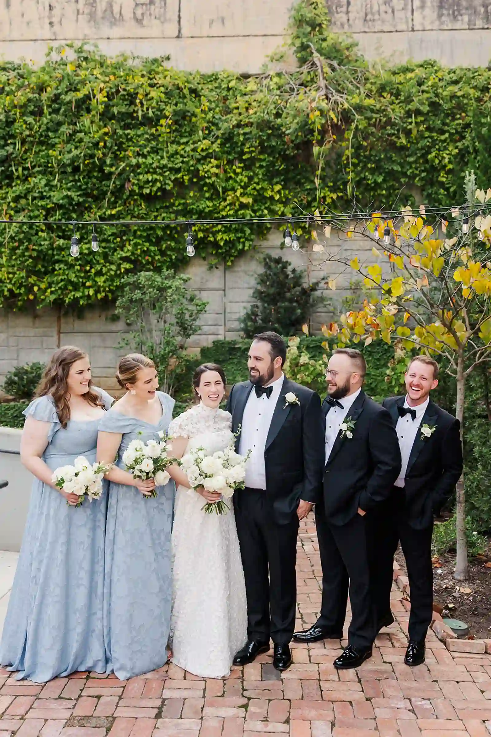 Wide wedding party portrait framed by ivy-covered walls and hanging lights
