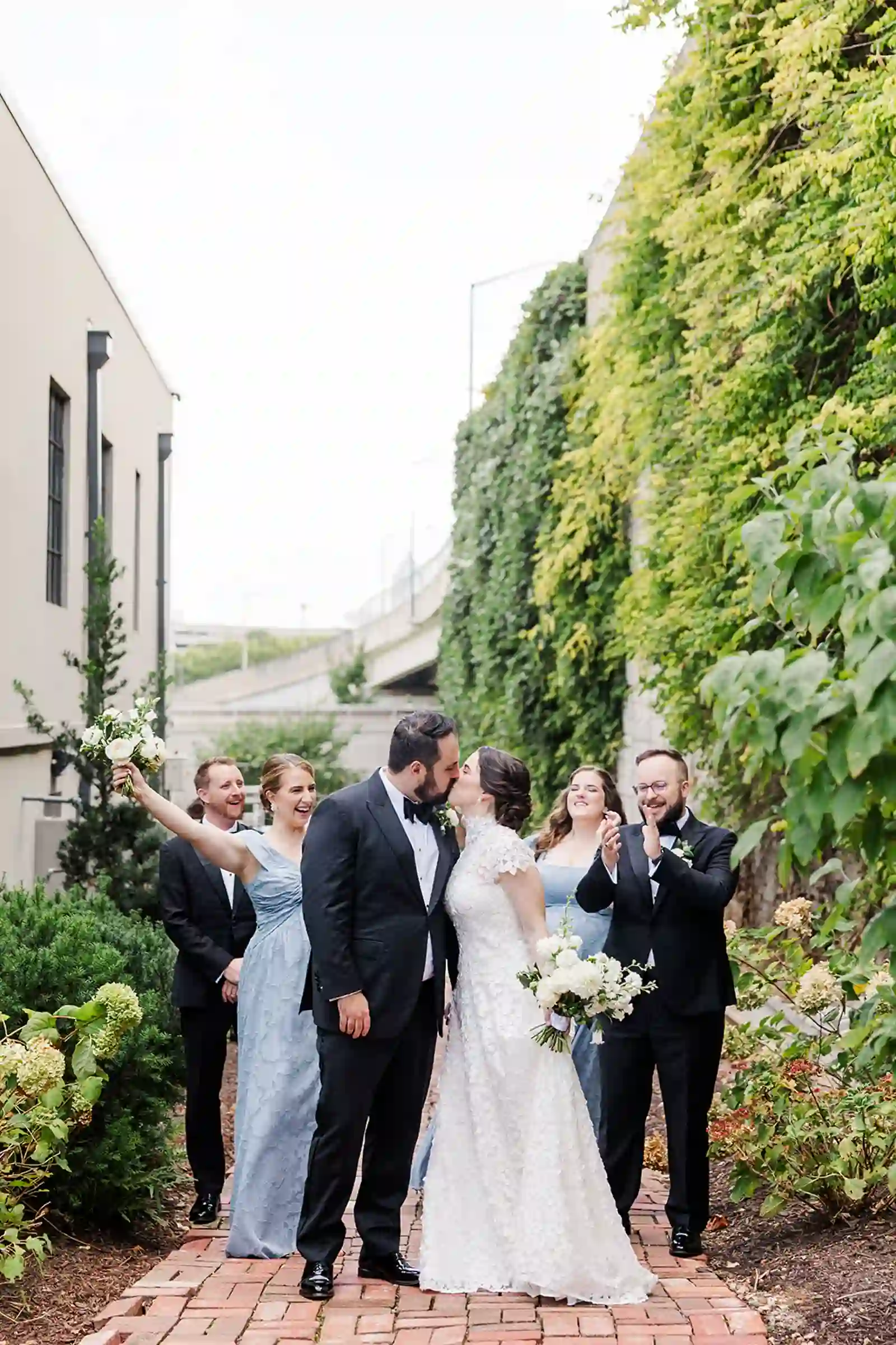 Bride and groom kissing on a brick pathway as the wedding party cheers beside them