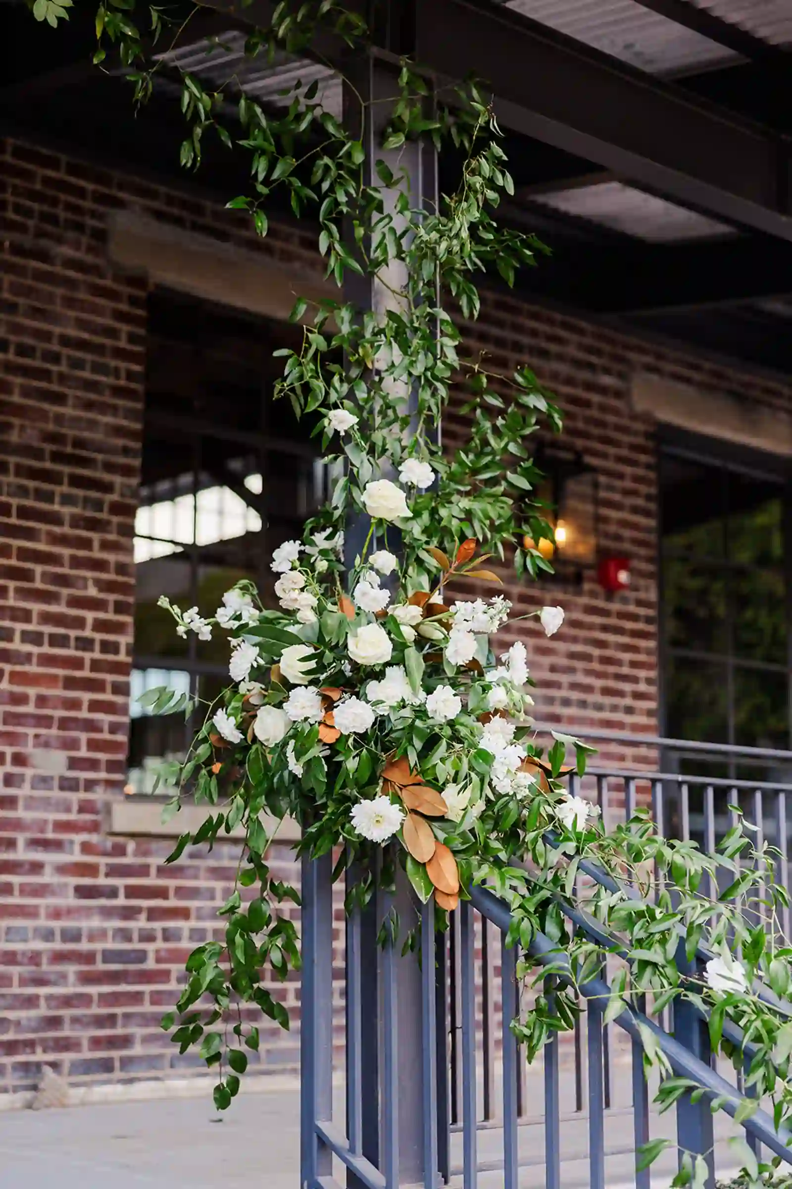 Lush white floral and magnolia installation climbing a steel column on the venue patio