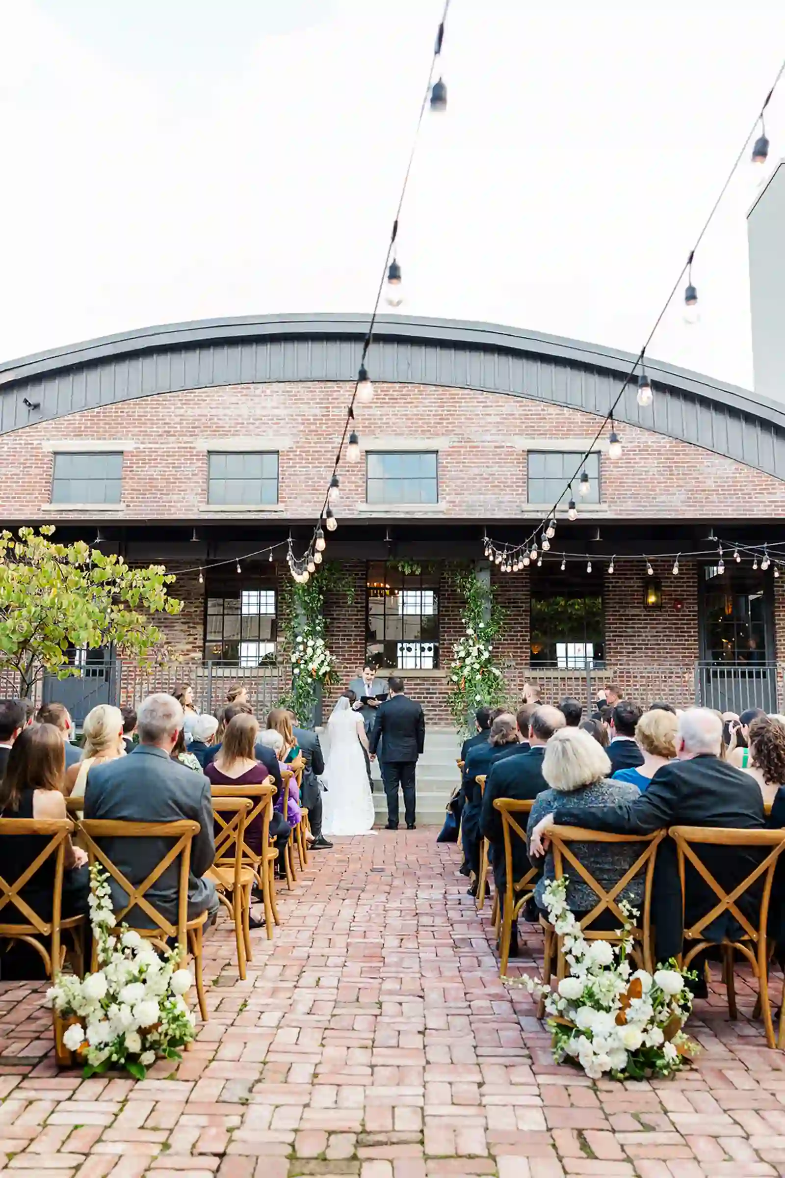 Wide view of the ceremony with guests seated beneath string lights at Bishop Station
