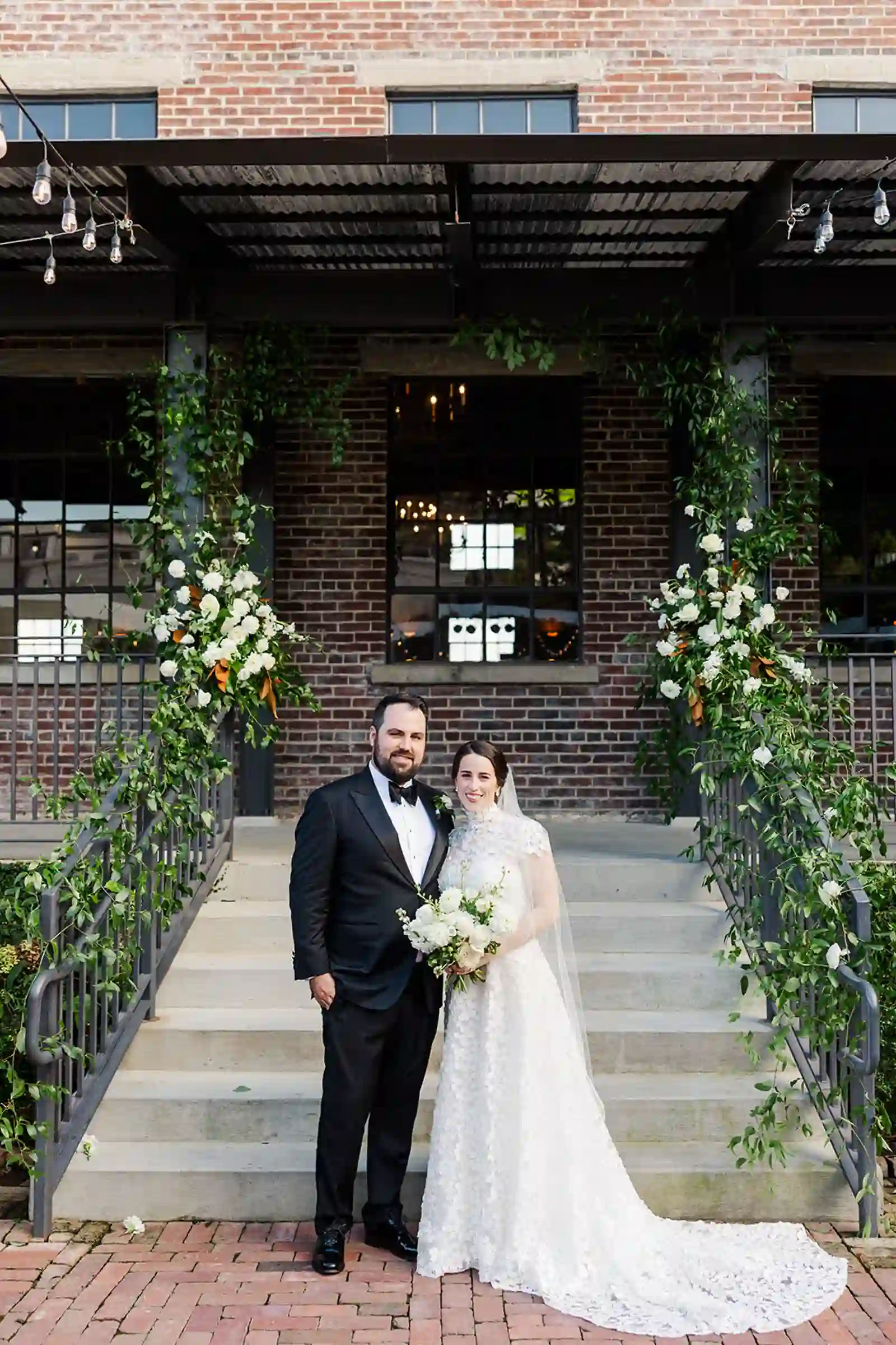 Formal portrait of the bride and groom on the venue's floral-draped steps