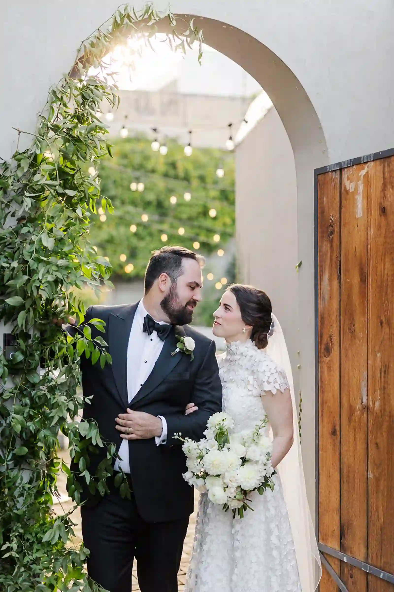 Romantic portrait of the couple framed by a greenery-draped archway at golden hour